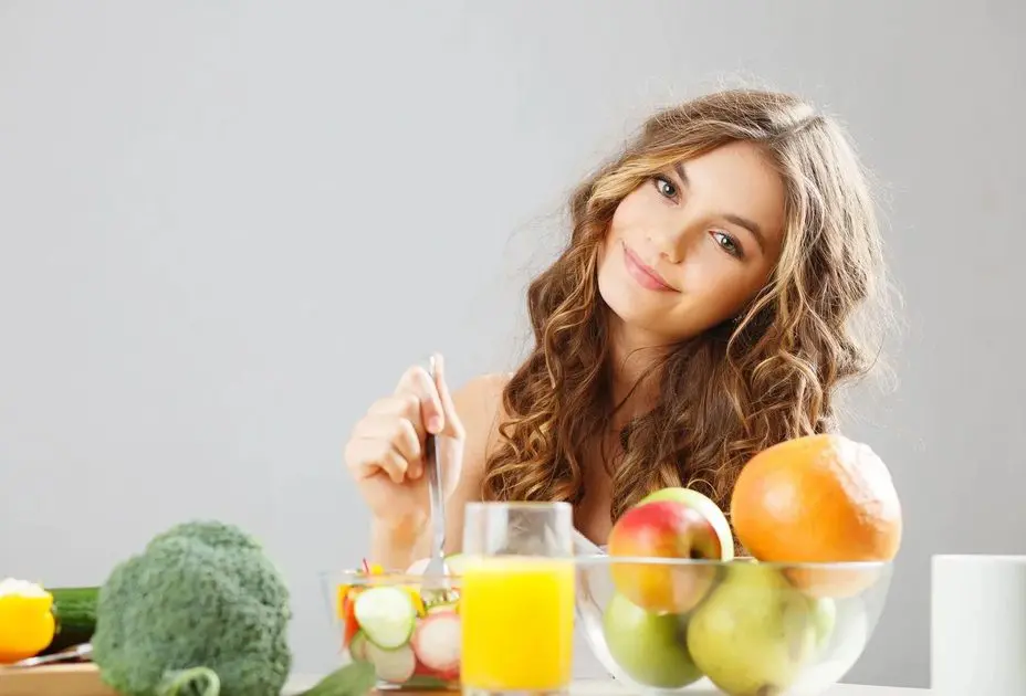 A woman sitting at the table with fruits and vegetables.